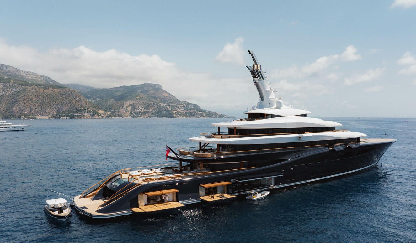 A superyacht at anchor off the Mediterranean coast, its tender alongside